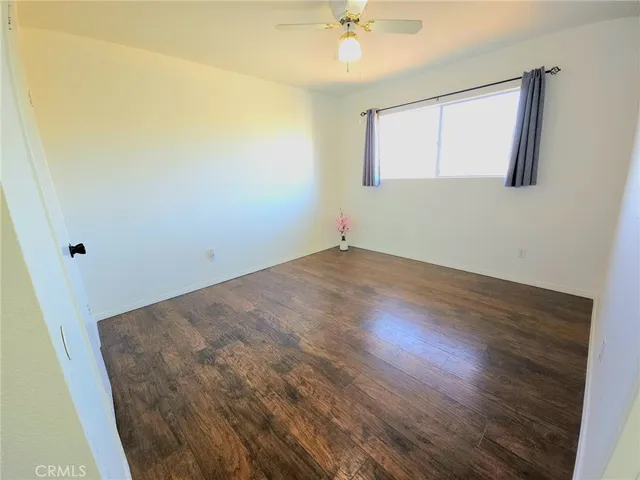 an empty room with wooden floor fan and windows