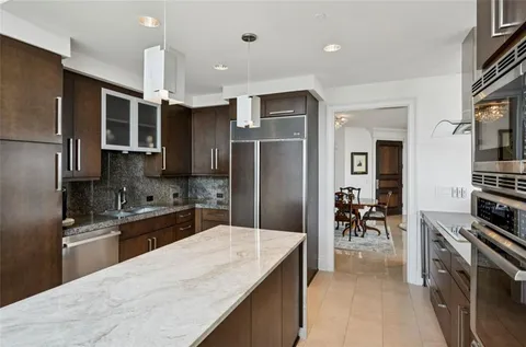 a kitchen with stainless steel appliances kitchen island granite countertop a refrigerator a stove a sink a dining table and chairs with wooden floor