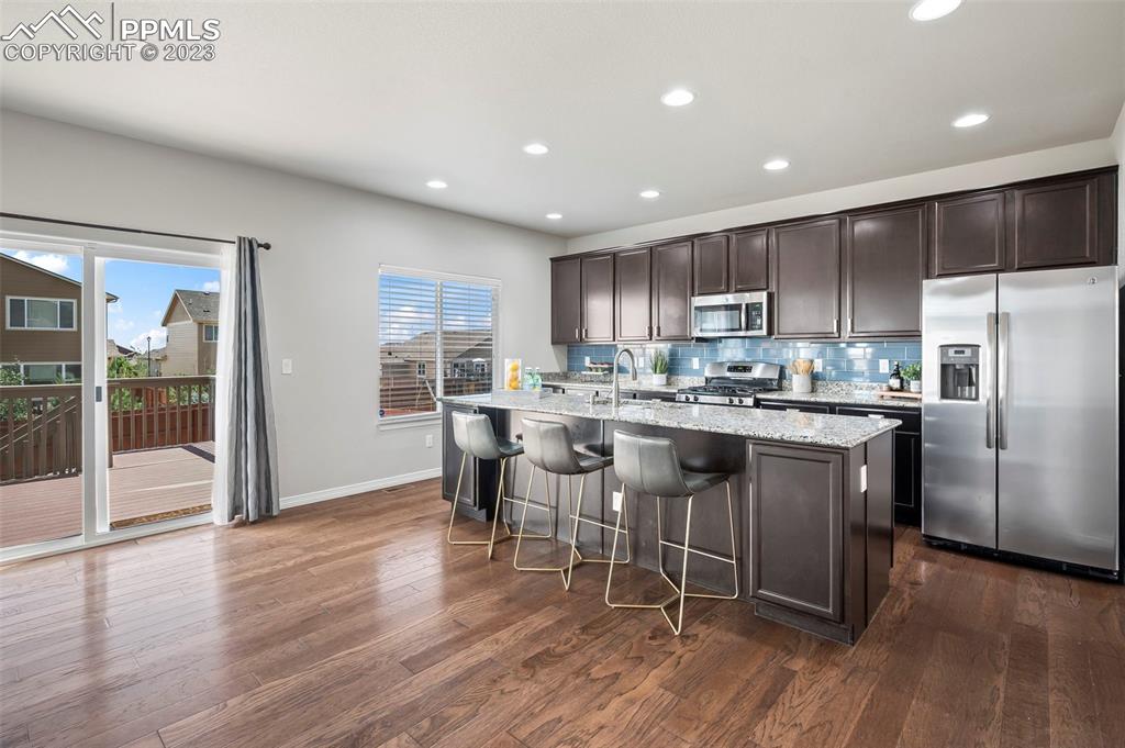 13232 Park Meadows Drive Peyton, CO 80831 - Photo 10 of 23 a kitchen with stainless steel appliances kitchen island granite countertop a refrigerator a stove a sink a dining table and chairs with wooden floor