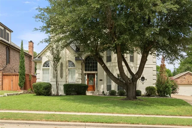 a view of a white house next to a yard with big trees