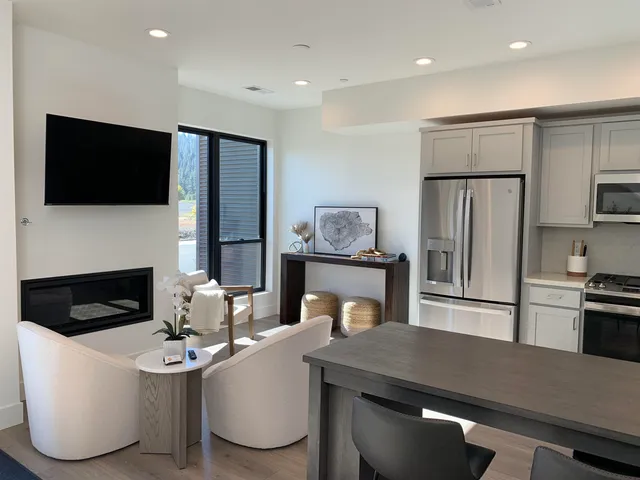 a living room with stainless steel appliances a fireplace a flat screen tv and a dining table