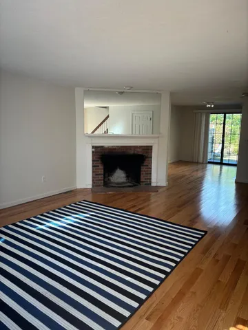 a view of an empty room with wooden floor fireplace and a window