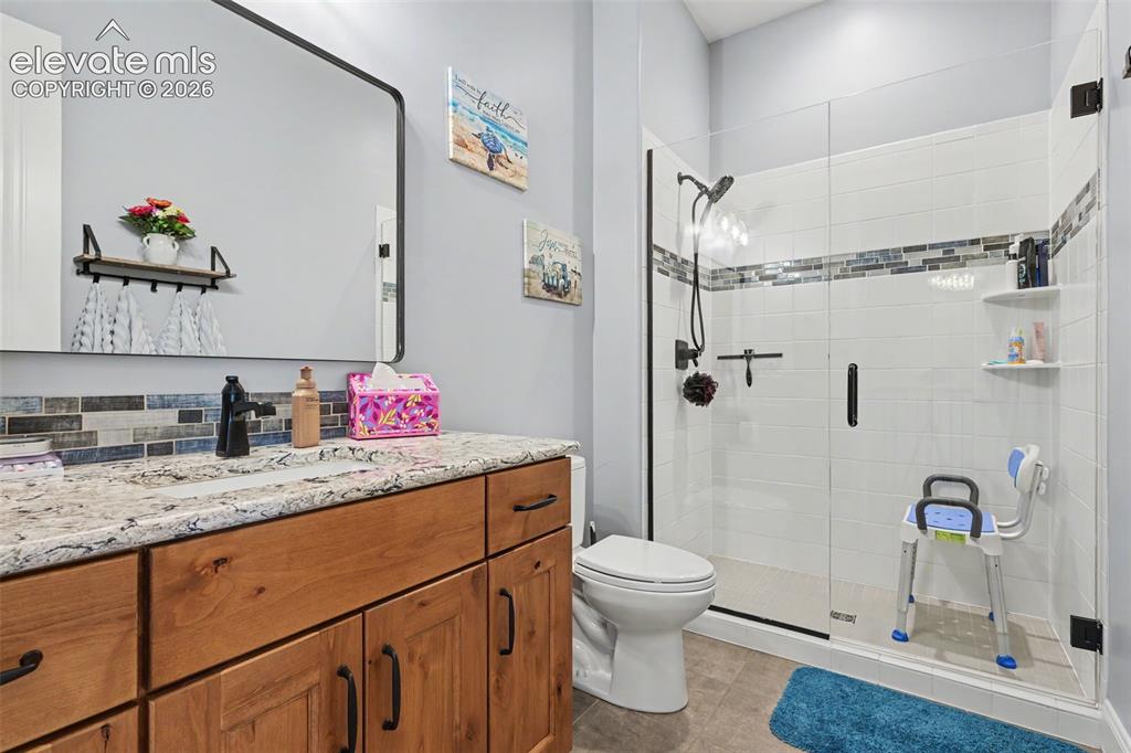21 Leaming Road Colorado Springs, CO 80906 - Photo 39 of 48 Bathroom featuring a wood-finish vanity with a light-toned countertop, a rectangular mirror, a glass-enclosed shower with subway tile, and a decorative tile accent band