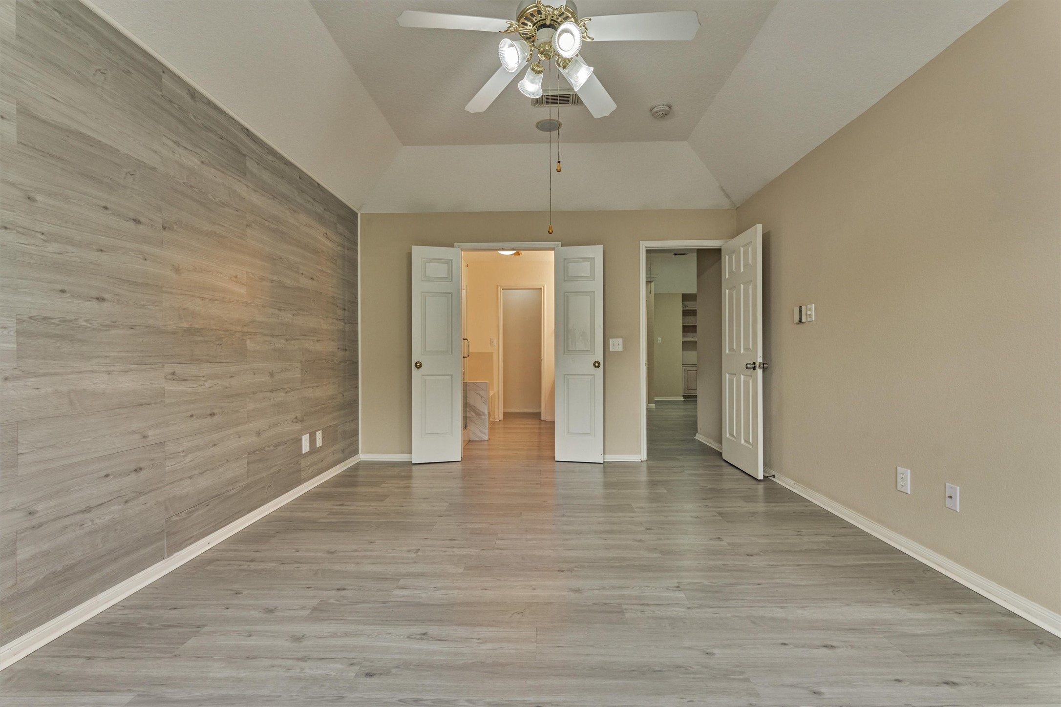 14420 Walters Road, Unit 26 Houston, TX 77014 - Photo 28 of 45 Bright, spacious primary bedroom with light gray flooring and a feature wall. It includes a ceiling fan and double doors leading to the bathroom, offering a modern and airy feel.