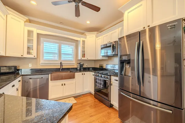 a kitchen with granite countertop a refrigerator a sink and white cabinets