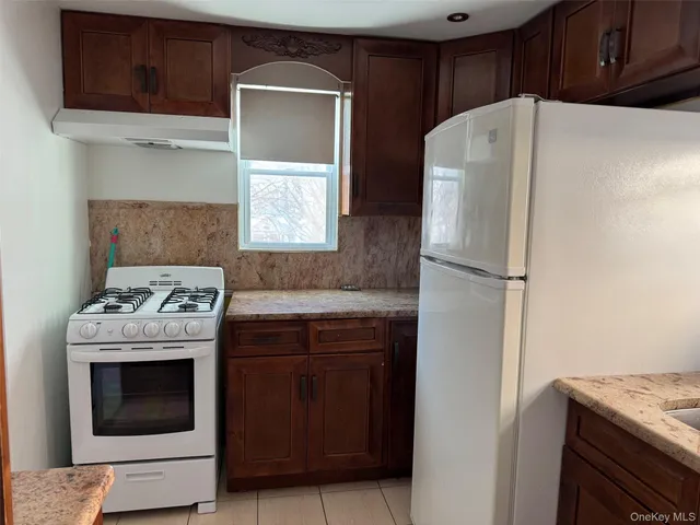a white refrigerator freezer and a stove sitting inside of a kitchen with granite countertop white cabinets