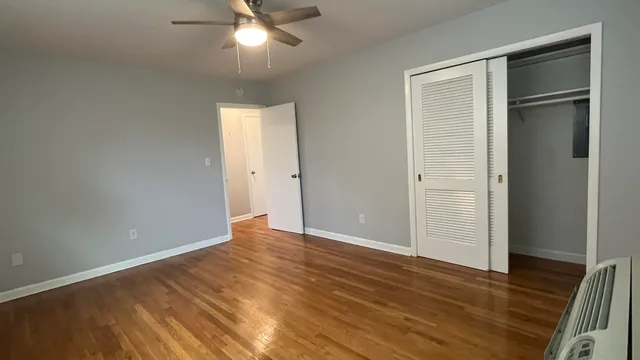 an empty room with wooden floor closet and fan