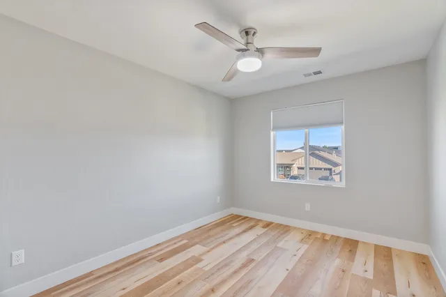 an empty room with wooden floor and ceiling fan
