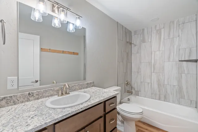 a bathroom with a granite countertop sink a toilet a mirror a bathtub and shower