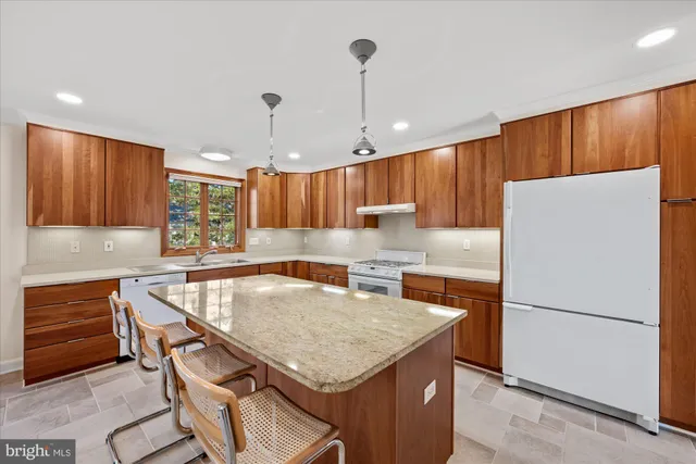 a kitchen with granite countertop a refrigerator a sink a stove a dining table and chairs