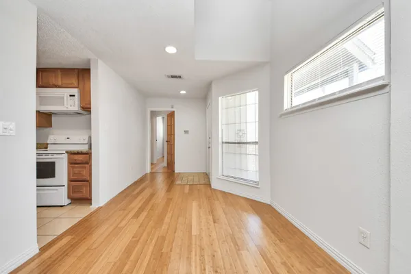 a view of empty room with wooden floor and kitchen