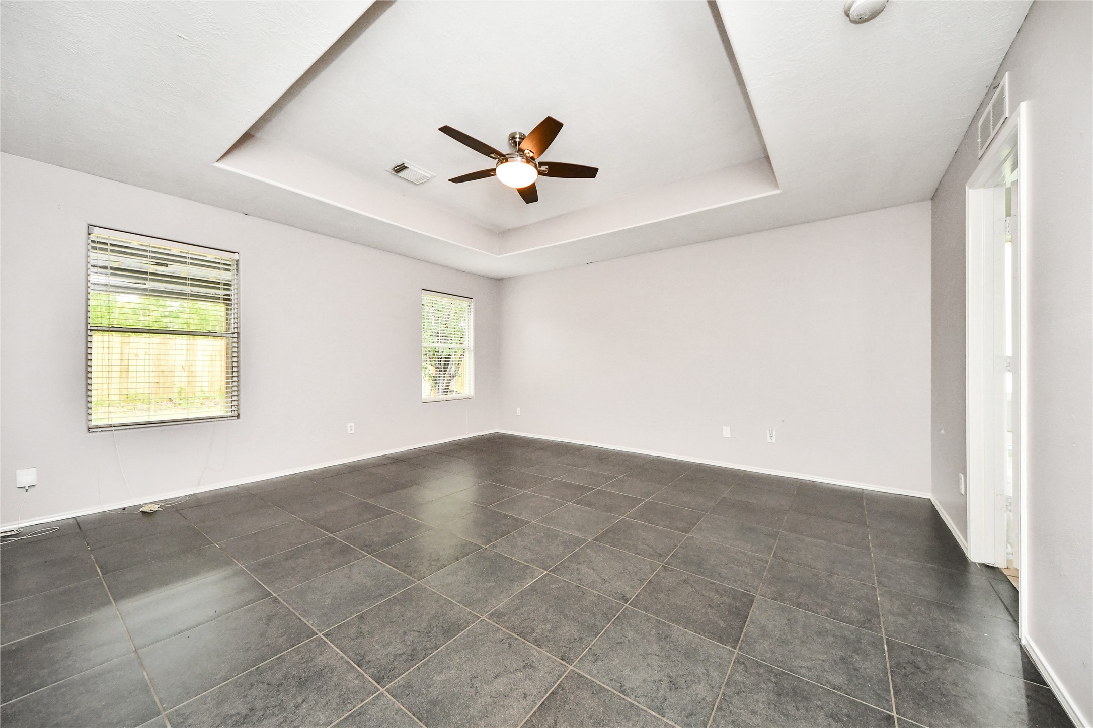 24019 Kingbriar Drive Spring, TX 77373 - Photo 27 of 41 The spacious primary bedroom features a sophisticated tray ceiling, dark tile flooring, and multiple windows, providing a serene retreat for relaxation at the end of the day.