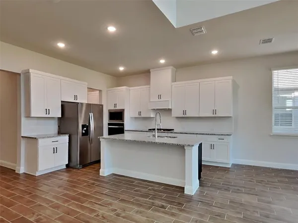 a kitchen with stainless steel appliances granite countertop a stove a refrigerator a sink a microwave and white cabinets with wooden floor