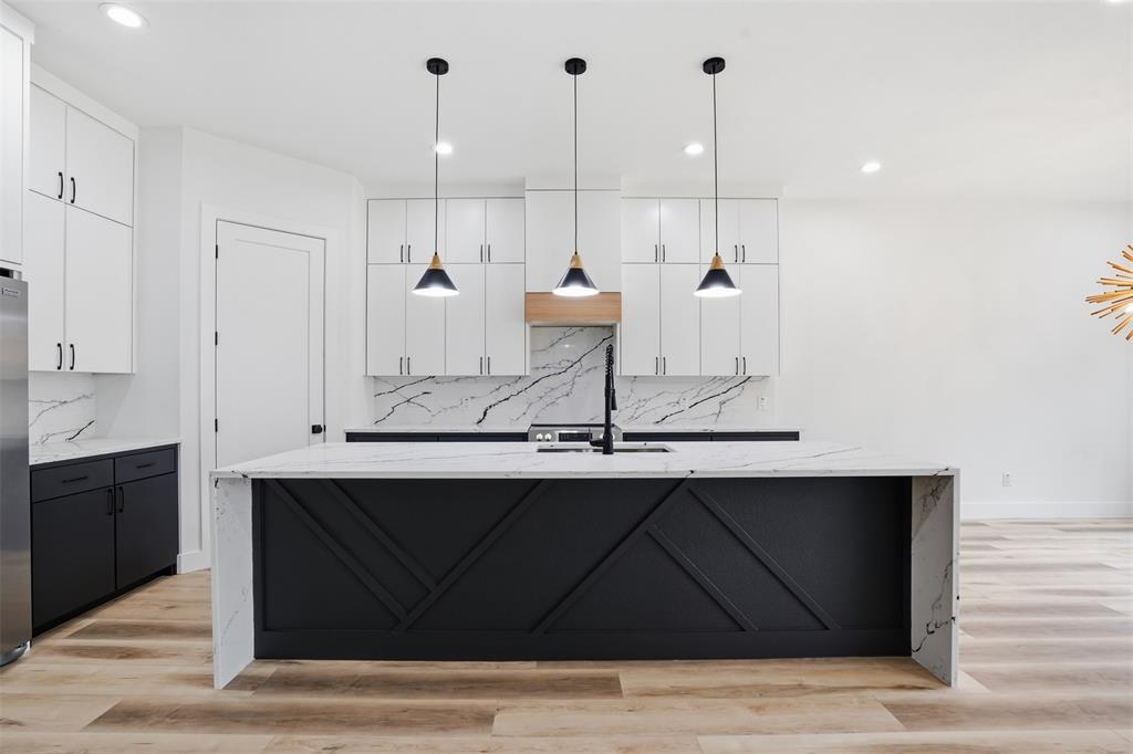 1111 Riverwood Road Dallas, TX 75217 - Photo 26 of 40 Spacious kitchen featuring a waterfall island with decorative paneling, white shaker cabinetry, black base cabinets, a built-in sink with a black faucet, and light wood-finish flooring