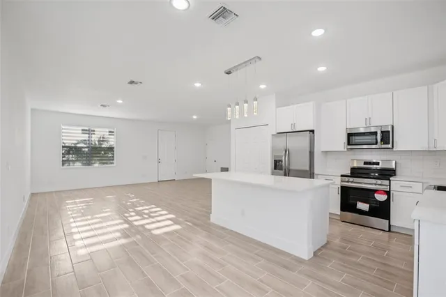 a large white kitchen with kitchen island a stove a sink a refrigerator and white cabinets with wooden floor