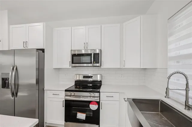 a kitchen with stainless steel appliances a refrigerator a stove a sink and white cabinets