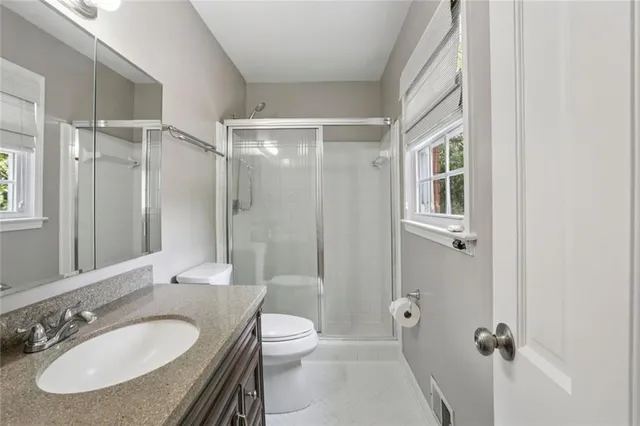 a bathroom with a granite countertop sink toilet a mirror a shower and a window