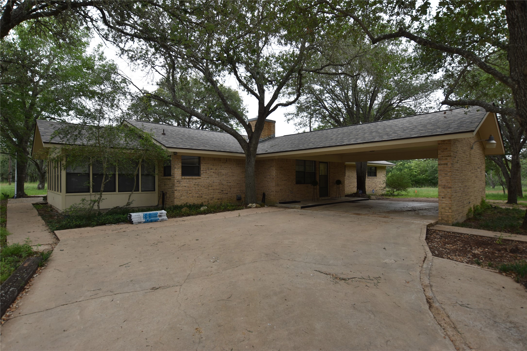 687 Fm 812 Road Red Rock, TX 78662 - Photo 2 of 40 Brick exterior residence featuring a 2 car covered carport, attached sunroom, mature trees, and a concrete driveway