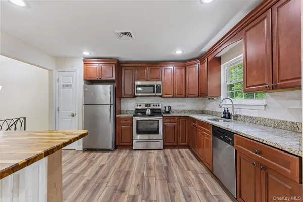 a kitchen with stainless steel appliances granite countertop a stove top oven a sink dishwasher and white cabinets with wooden floor