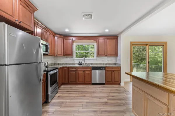 a kitchen with stainless steel appliances granite countertop a refrigerator a sink dishwasher a stove with wooden cabinets and floor