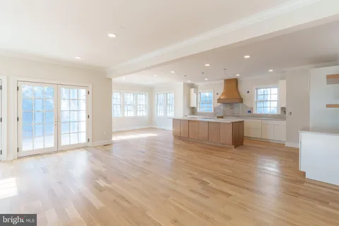 a view of an empty room with wooden floor and a kitchen