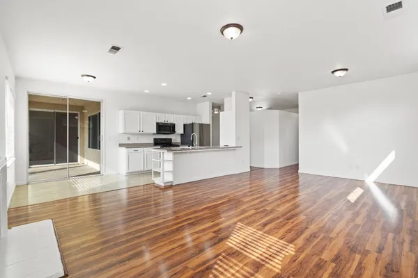 an empty room with wooden floor and kitchen view