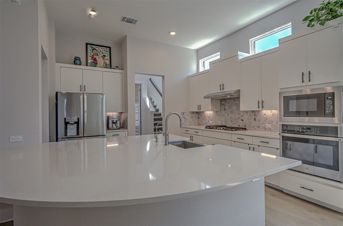 a kitchen with stainless steel appliances a stove top oven a sink a refrigerator and white cabinets