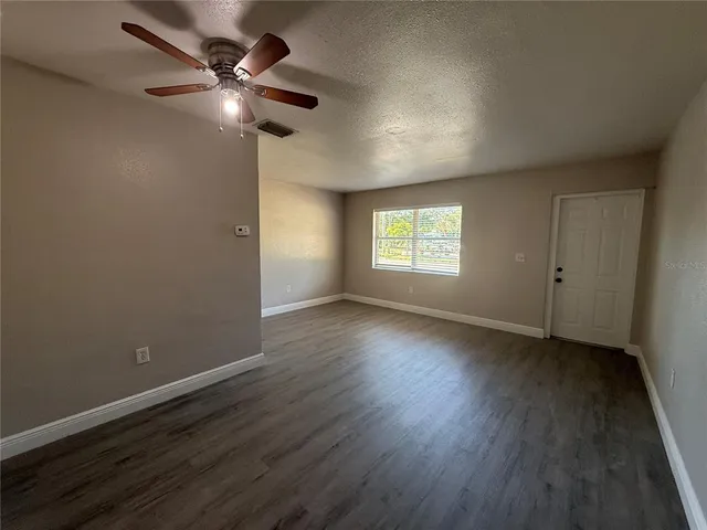 an empty room with wooden floor fan and windows