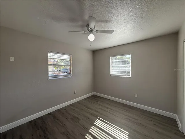 an empty room with wooden floor ceiling fan and windows
