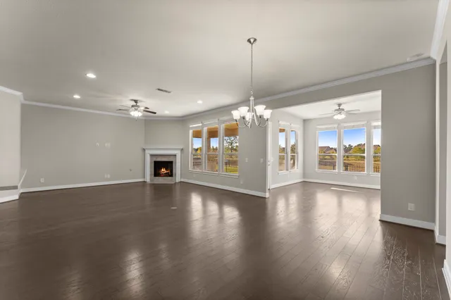 a view of an empty room with wooden floor kitchen view and a window
