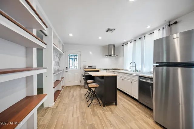 a kitchen with stainless steel appliances granite countertop a refrigerator a sink dishwasher a stove and white countertops with wooden floor