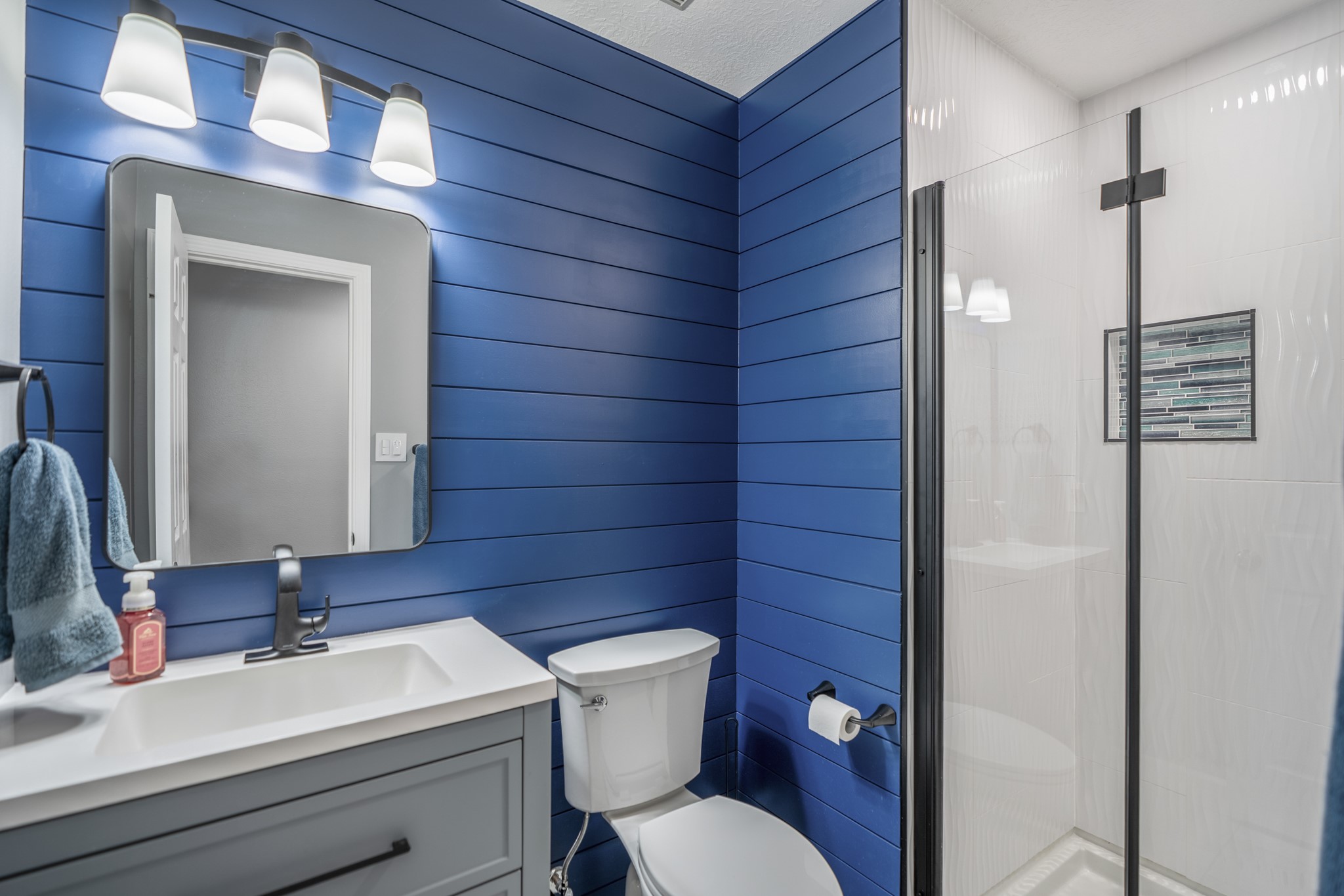 3411 Utah Beach Court Spring, TX 77388 - Photo 32 of 50 This bath adds a bold pop of color with deep blue shiplap-style walls, a gray vanity, modern lighting, and a glass-enclosed shower with a tiled niche.