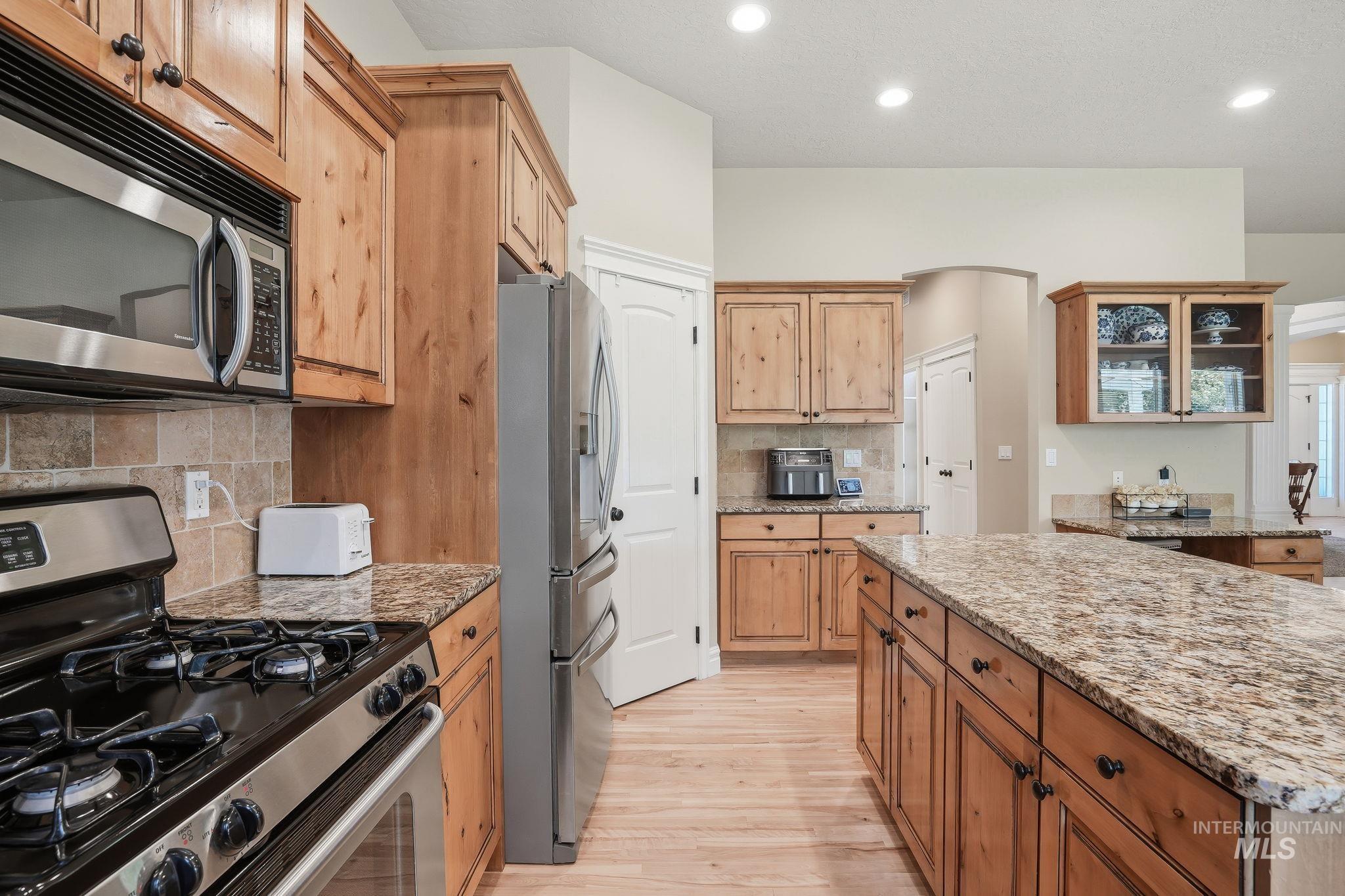 3969 North Hollymount Way Meridian, ID 83646 - Photo 14 of 47 Kitchen featuring wood cabinetry, stainless steel appliances, a large center island with a stone countertop, a stone tile backsplash, and recessed lighting