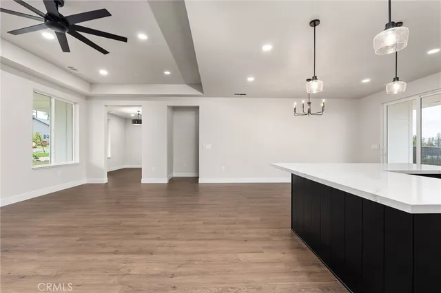 a view of an empty room and kitchen with a ceiling fan wooden floor