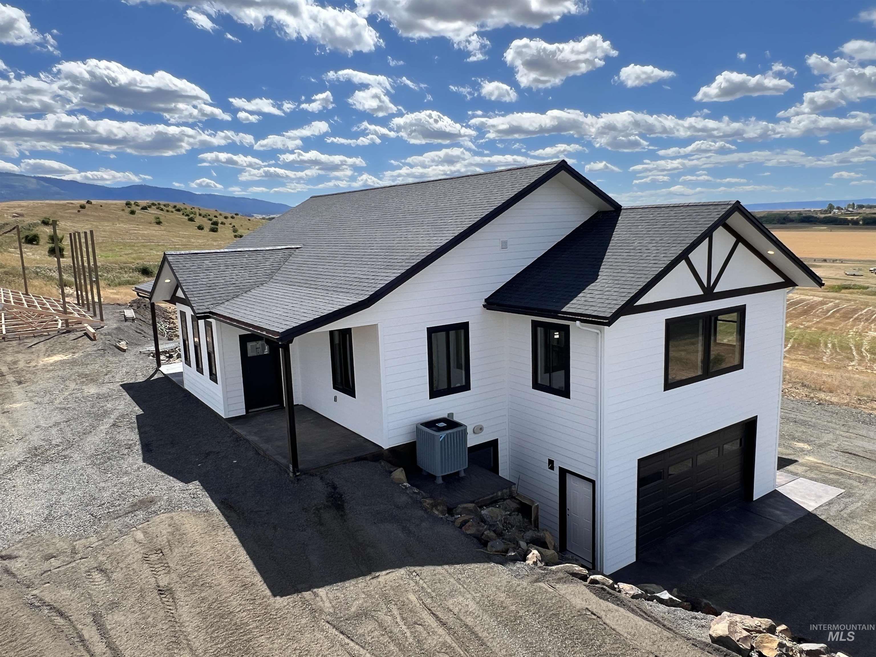 View of property exterior featuring a shingled roof, a garage, driveway, and a rural view
