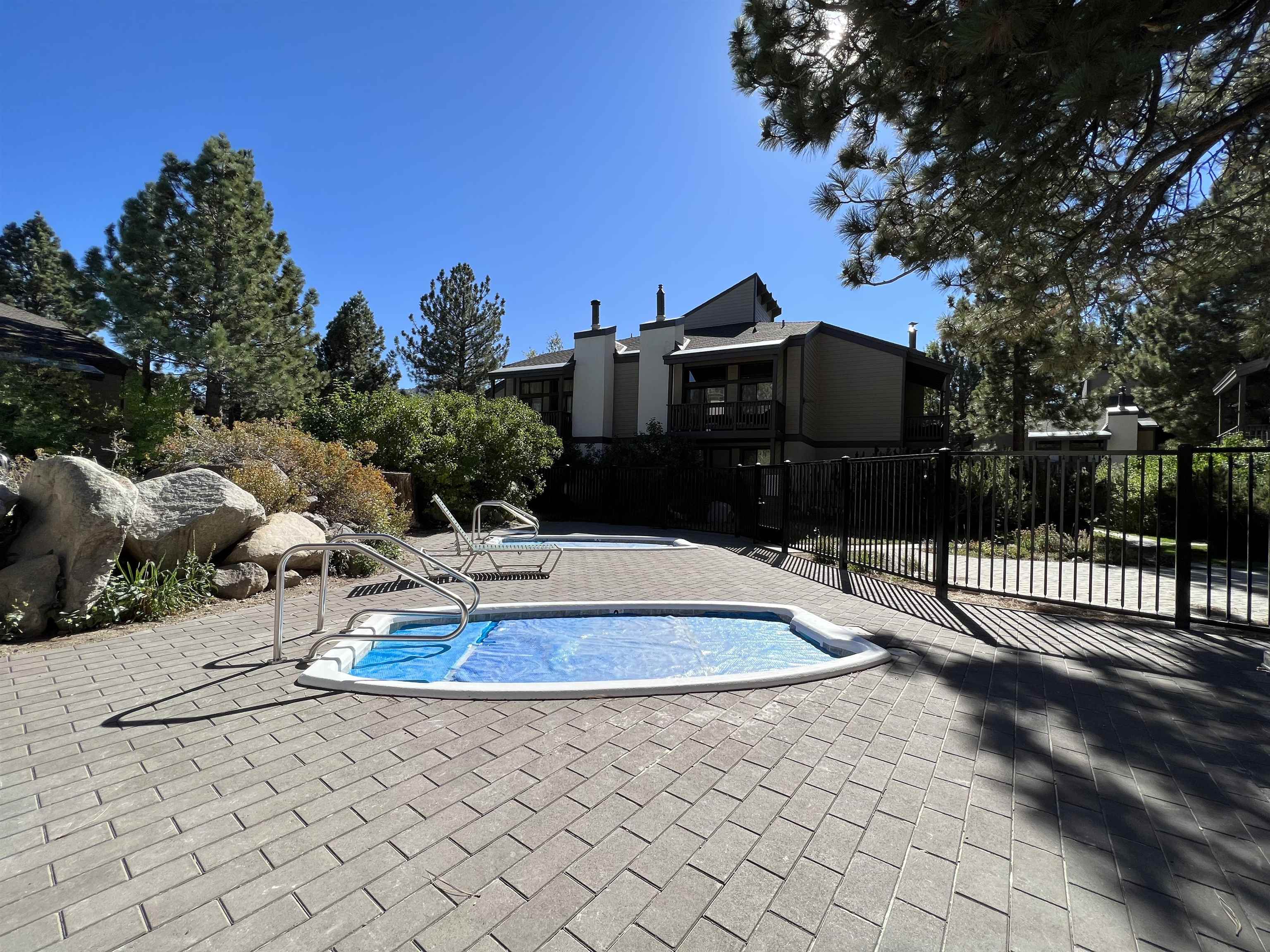 362 Old Mammoth Road, Unit 59 Mammoth Lakes, CA 93546 - Photo 31 of 35 Outdoor spa with integrated steps and handrails, surrounded by paver patio, mature landscaping, and a privacy fence