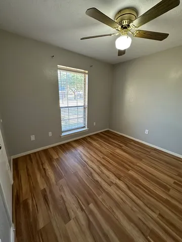 an empty room with wooden floor fan and windows