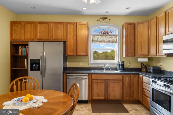 a kitchen with stainless steel appliances granite countertop a refrigerator a sink a stove a dining table and chairs with wooden floor