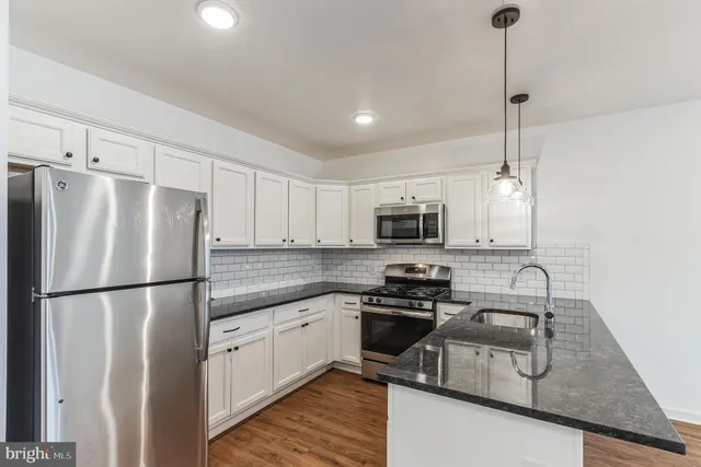 a kitchen with stainless steel appliances granite countertop a refrigerator a sink dishwasher a s stove top oven a refrigerator and white cabinets with wooden floor