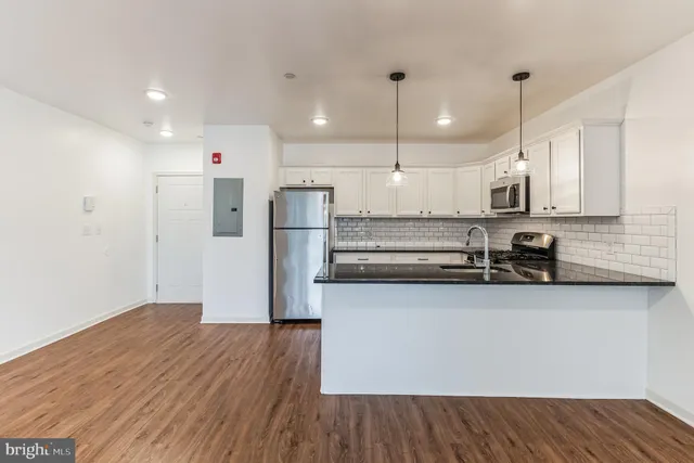 a kitchen with stainless steel appliances granite countertop a refrigerator a sink dishwasher a stove and white countertops with wooden floor