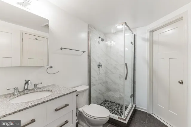 a bathroom with a granite countertop sink toilet a mirror a vanity and shower