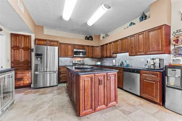 a kitchen with stainless steel appliances granite countertop a stove top oven a sink dishwasher a refrigerator and a refrigerator with wooden cabinets