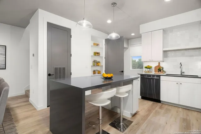 a kitchen with stainless steel appliances kitchen island granite countertop a sink a stove a refrigerator and white cabinets with wooden floor