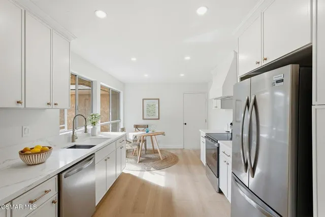 a kitchen with stainless steel appliances a refrigerator a sink a stove and white cabinets