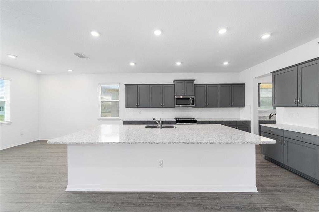 7232 Southwest 63rd Street Ocala, FL 34474 - Photo 18 of 54 a large white kitchen with kitchen island a stove a sink a refrigerator and white cabinets with wooden floor