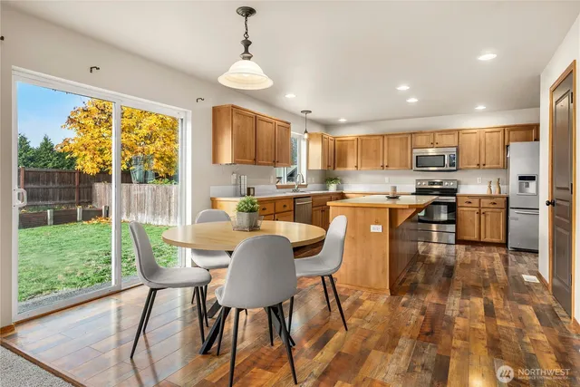 a kitchen with stainless steel appliances granite countertop a stove top oven a sink dishwasher a dining table and chairs with wooden floor