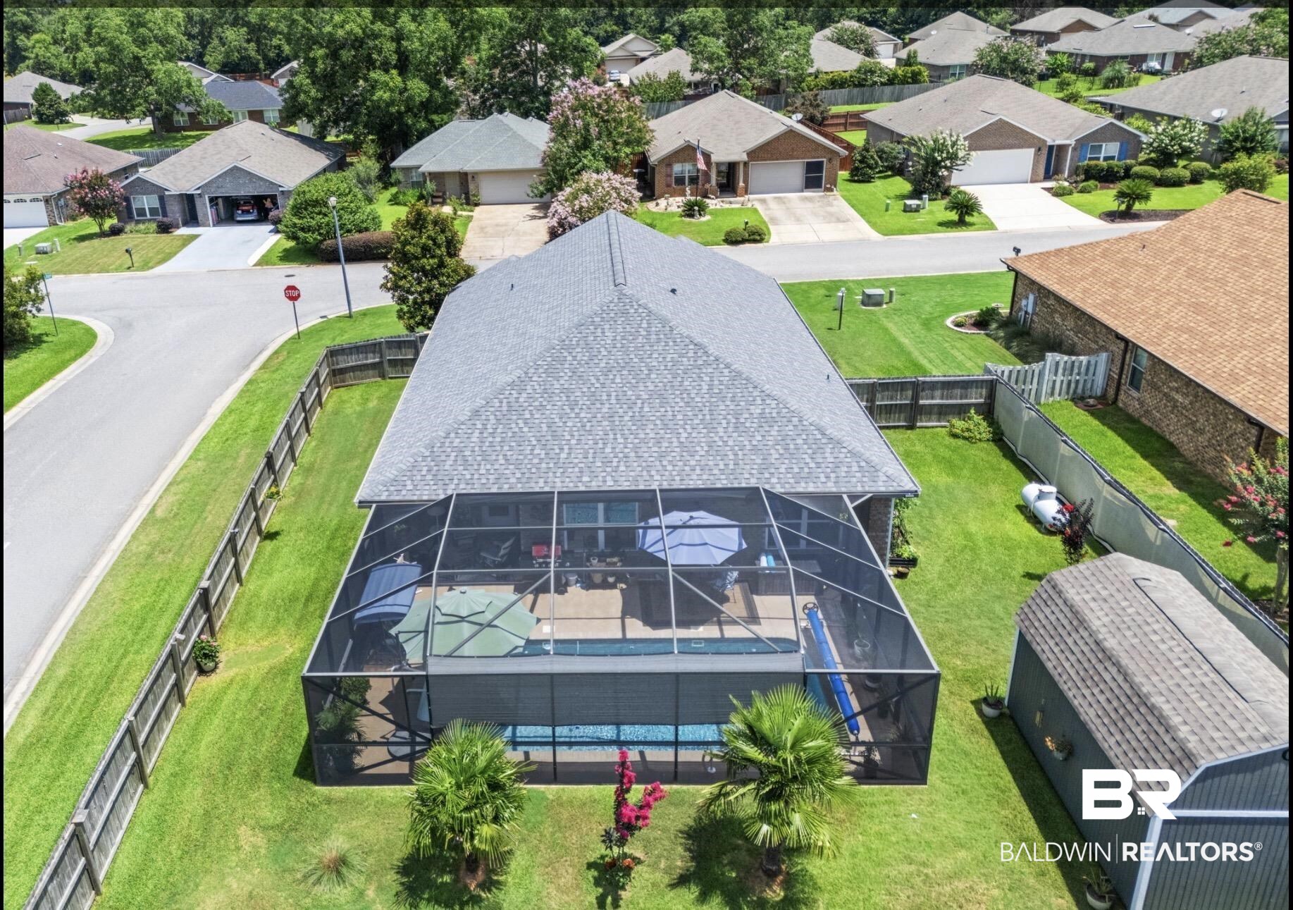 1676 Abbey Loop Foley, AL 36535 - Photo 26 of 31 Screened-in pool area featuring a paved deck, mature palm trees, and a shingled roofline