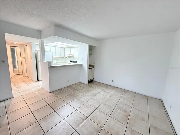 an empty room with windows and view of kitchen