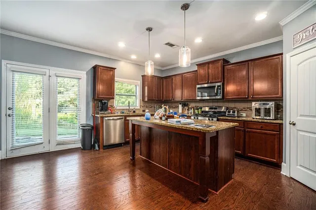 a kitchen with stainless steel appliances granite countertop a stove a sink dishwasher a refrigerator and a dining table with wooden floor