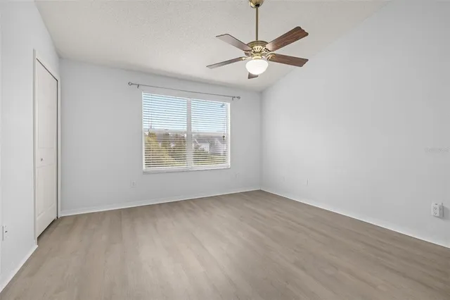 an empty room with wooden floor ceiling fan and windows